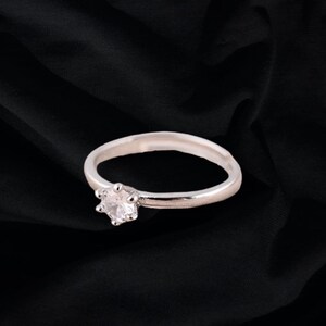 May include: A silver ring with a single clear stone set in a prong setting.