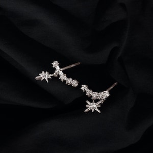 May include: A pair of silver earrings with a star design. The earrings are made of a curved bar with a star dangling from the end.