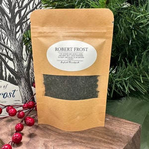 Puede incluir: Una bolsa de papel marrón con una ventana transparente que muestra té de hoja suelta en su interior. La bolsa tiene una etiqueta blanca con el texto "ROBERT FROST" y una cita del poeta. El texto de la etiqueta dice: "The woods are lovely, dark and deep, But I have promises to keep, And miles to go before I sleep." La etiqueta también incluye el texto "Splash Breakfast".