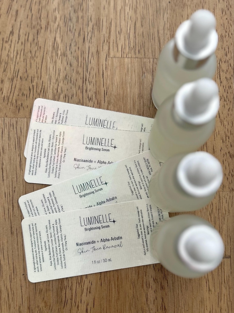 Puede incluir: Cuatro frascos cuentagotas de vidrio esmerilado dispuestos en una fila vertical, cada uno con una etiqueta blanca rectangular. Las etiquetas muestran el texto Luminelle Brightening Serum, Niacinamide + Alpha-Arbutin, Skin Tone Renewal y 30 ml.