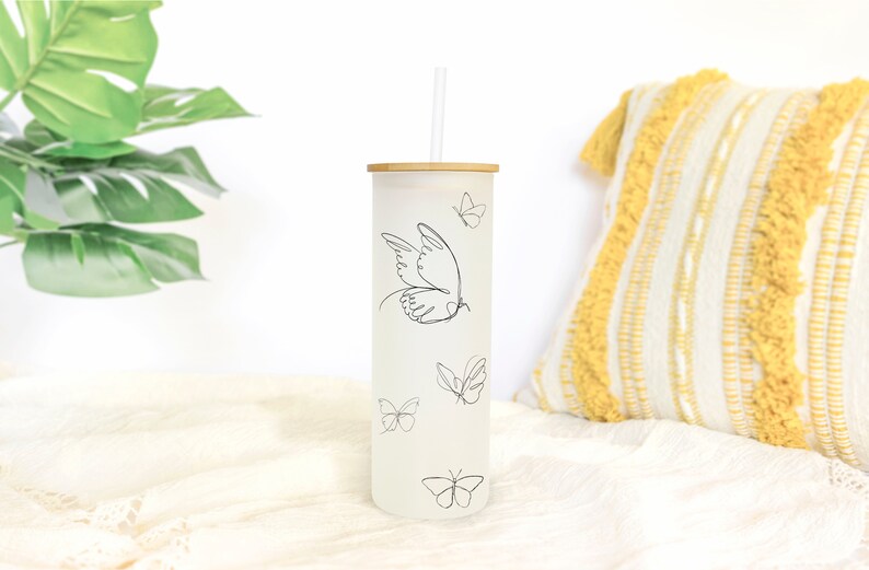 May include: A white frosted tumbler with a bamboo lid and a black line drawing of a butterfly. The tumbler has a straw and is decorated with several butterflies.
