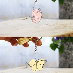 May include: Two clear acrylic keychains with a butterfly design. The top keychain features a pink butterfly with black outlines. The bottom keychain features a yellow butterfly with black outlines.