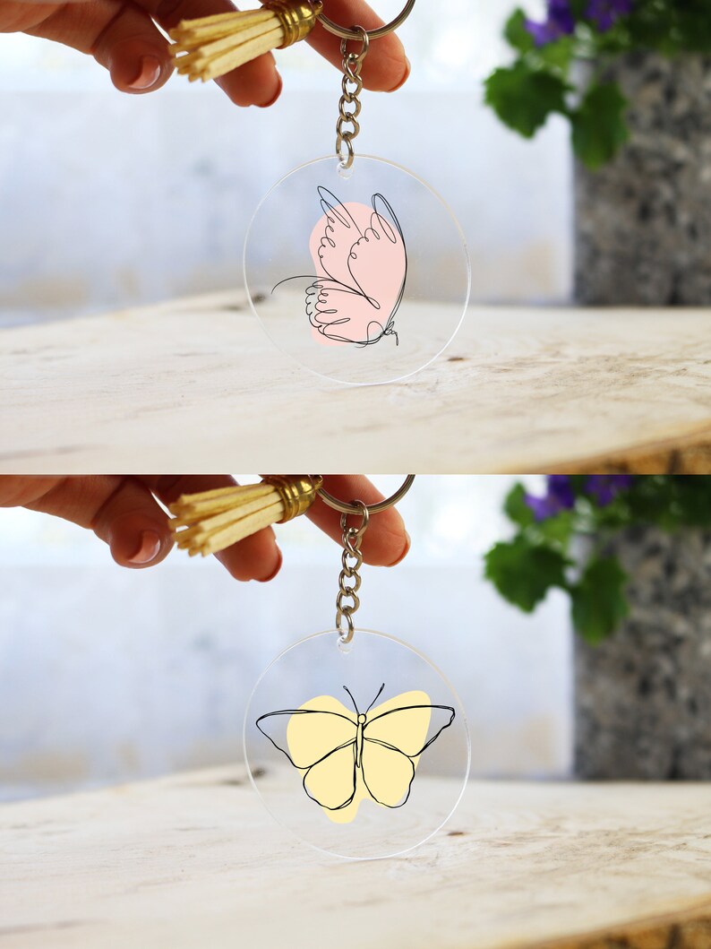 May include: Two clear acrylic keychains with a butterfly design. The top keychain features a pink butterfly with black outlines. The bottom keychain features a yellow butterfly with black outlines.