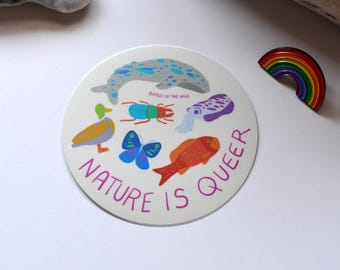 May include: A white round sticker with a colorful illustration of a whale, a beetle, a squid, a butterfly, a duck, and a fish. The text "Nature is Queer" is written in pink around the edge of the sticker. The text "Ripple in the Wild" is written in black at the top of the sticker.