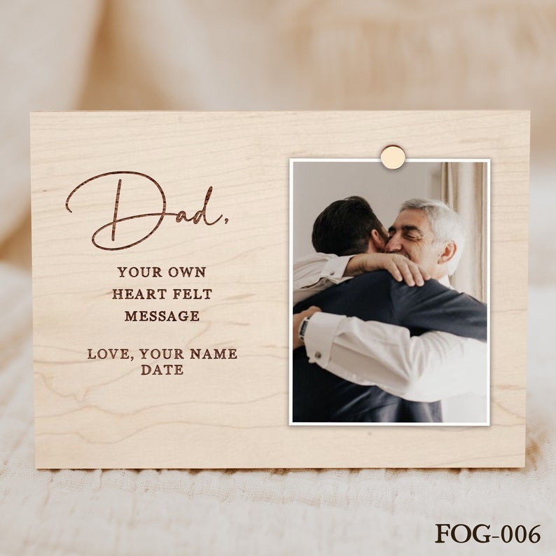 Puede incluir: Un marco de fotos de madera con un acabado de madera marr&oacute;n claro. El marco tiene un recorte para una foto y un espacio para un mensaje personalizado. El mensaje dice "Pap&aacute;, Tu propio mensaje del coraz&oacute;n Amor, Tu nombre Fecha".