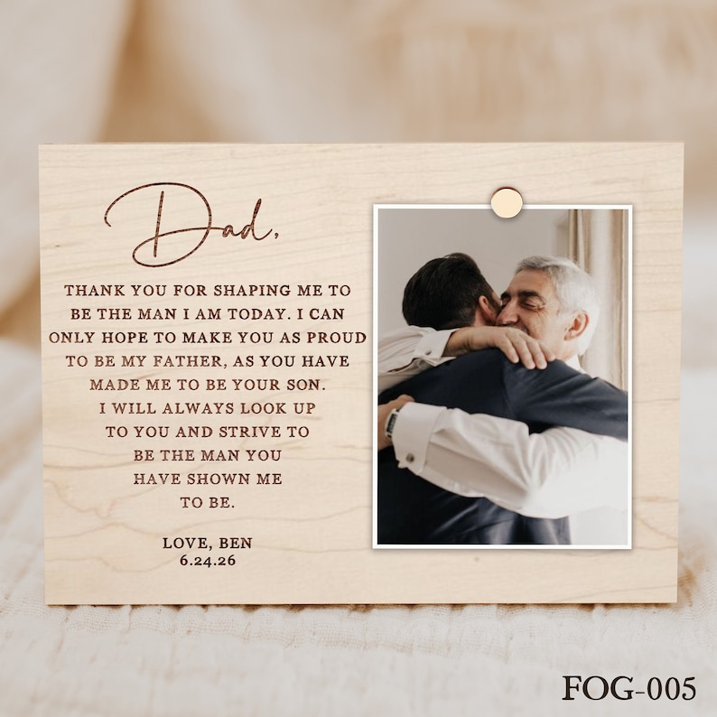 Puede incluir: Una placa de madera con un mensaje escrito a mano a un padre de parte de su hijo. El mensaje dice: "Pap&aacute;, Gracias por darme forma para ser el hombre que soy hoy. Solo puedo esperar hacerte tan orgulloso de ser mi padre como t&uacute; me has hecho de ser tu hijo. Siempre mirar&eacute; hacia ti y me esforzar&eacute; por ser el hombre que me has mostrado ser. Con amor, Ben 6.24.26". Una foto del hijo abrazando a su padre est&aacute; en la esquina superior derecha de la placa.