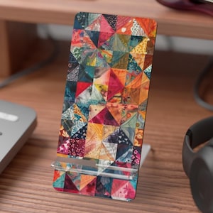 May include: A colorful phone stand with a patchwork design. The stand is made of a clear material and has a black base. The stand is on a wooden surface.
