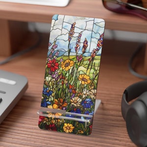May include: A stained glass phone stand with a floral design featuring yellow, red, blue, and green flowers. The stand is made of clear acrylic and has a metal base.