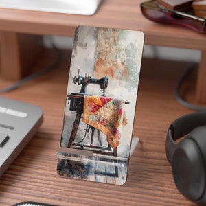 May include: A vintage sewing machine with a colorful quilt on the table, painted in a watercolor style. The image is printed on a phone stand.