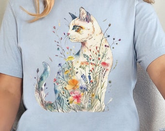 May include: A light blue t-shirt with a watercolor illustration of a cat sitting in a field of flowers. The cat is white with black and brown markings. The flowers are in shades of pink, yellow, and blue.