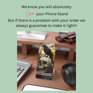 May include: A phone stand with a stained glass design featuring a skull and a raven. The stand is made of metal and has a black base.