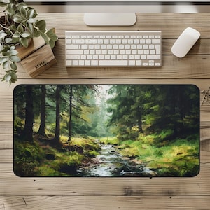 May include: A rectangular desk mat featuring a forest scene with a stream. The artwork depicts tall green trees, lush green grass, and a flowing stream. The mat is on a wooden desk with a keyboard, mouse, and plant.