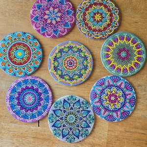 May include: Eight round coasters with colorful mandala designs. Each coaster features a different pattern of blue, green, pink, yellow, and red beads.