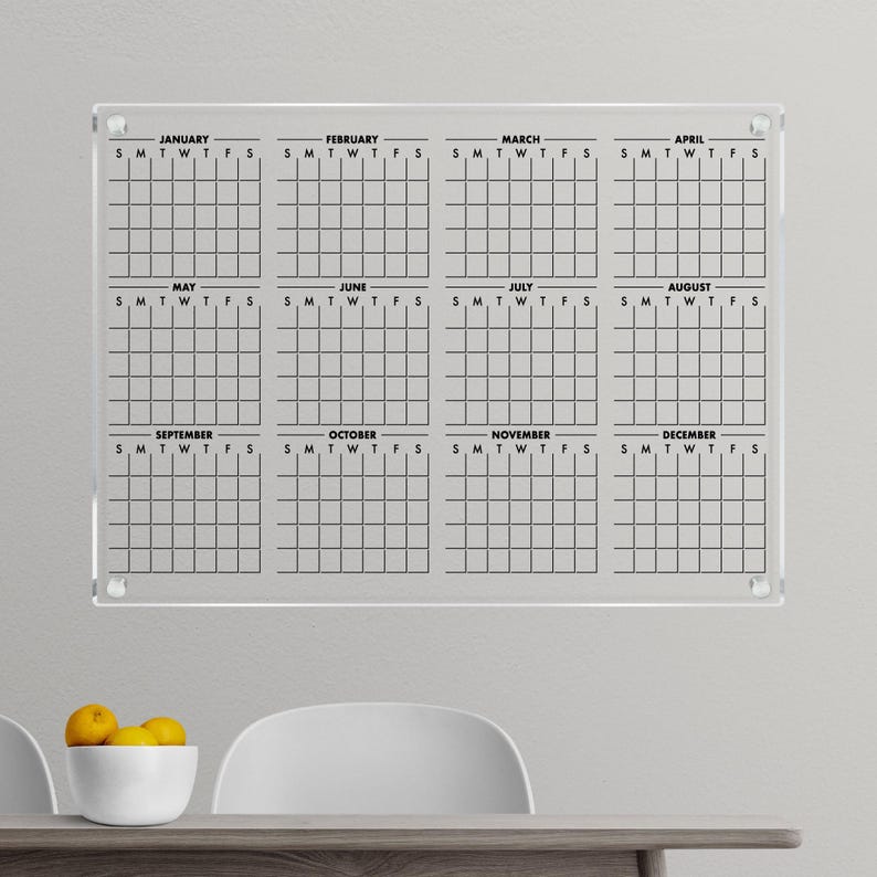 May include: A clear acrylic dry-erase calendar with a grid layout for each month of the year. The calendar is labelled with the months January through December and the days of the week, Sunday through Saturday.