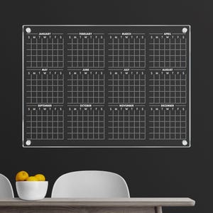 May include: A clear acrylic dry-erase calendar with a grid for each month of the year. The calendar is labelled with the months January through December and the days of the week, Sunday through Saturday.