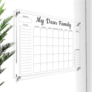 以下が含まれることがあります： 「My Dear Family」という文字が書かれた透明なアクリル製のドライイレースカレンダー。カレンダーには、週ごとの曜日、やることリスト、メモ、食料品のためのスペースがあります。