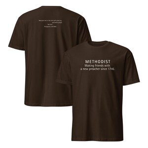 May include: A brown short-sleeved t-shirt featuring white text on the front that reads METHODIST Making friends with a new preacher since 1746. The back of the shirt displays the text Welcome him in the Lord with great joy, and honour people like him. Philippians 2:29 (NIV).