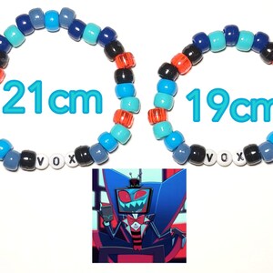 May include: Two beaded bracelets, one 21cm and the other 19cm, feature a mix of blue, black, orange, and white beads spelling "VOX". A cartoon image of a character in a suit is in the lower corner.