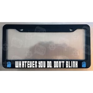 May include: Black license plate frame with a white graphic that says "WHATEVER YOU DO, DON'T BLINK" and two blue TARDIS silhouettes on either side.