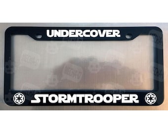 Puede incluir: Marco de matrícula negro con texto blanco que dice "Undercover Stormtrooper" y un símbolo imperial blanco a cada lado.