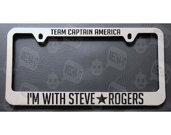 May include: A silver metal license plate frame with the text "TEAM CAPTAIN AMERICA" at the top and "I'M WITH STEVE ROGERS" at the bottom. A black star is between the words "STEVE" and "ROGERS".