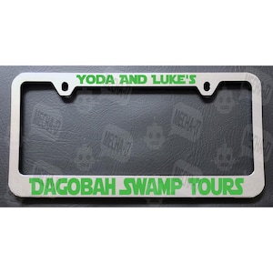 May include: A silver license plate frame with green text that reads "YODA AND LUKE'S DAGOBAH SWAMP TOURS".