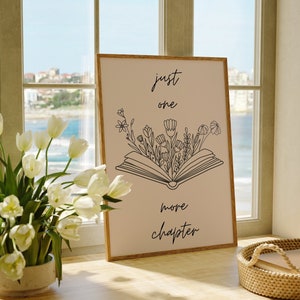 May include: A beige framed print with black text and a line drawing of an open book with flowers growing from it. The text reads "just one more chapter".
