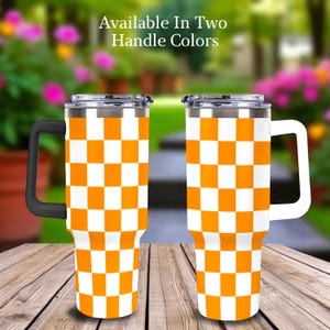 Puede incluir: Dos tazas de viaje de acero inoxidable con un patrón de cuadros blancos y naranjas. Una taza tiene un asa negra y la otra un asa blanca. El texto "Available In Two Handle Colors" está en la parte superior.