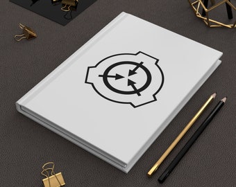 Op de afbeelding: Een wit notitieboek met een zwart-wit logo van een cirkel met pijlen die in verschillende richtingen wijzen. Het notitieboek ligt op een donkergrijze ondergrond met twee potloden en gouden paperclips.