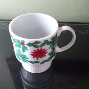 May include: White ceramic mug with a Christmas holly and poinsettia design. The mug has a handle and a base.