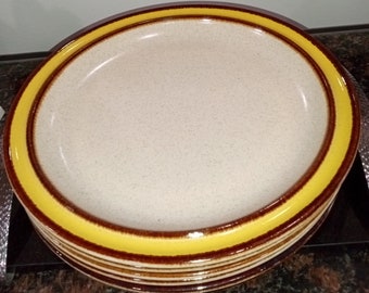 Puede incluir: Una pila de platos de cerámica marrones y amarillos. El plato superior tiene un borde amarillo y una banda marrón.