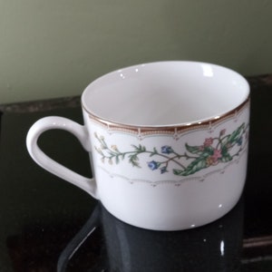 May include: A white teacup with a floral pattern in shades of green, blue, and pink. The cup has a gold rim and a delicate floral design.