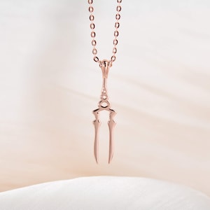 May include: A rose gold necklace with a delicate, double-pronged pendant. The pendant is shaped like a stylized sword or dagger.