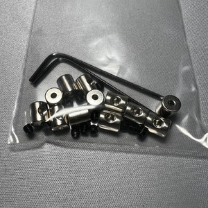 May include: A close-up of a bag containing a set of silver metal fasteners and a small black wrench.