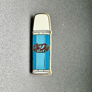 May include: A blue and white metal pin shaped like a can of Old Dutch potato chips. The can has a gold trim and the words "Old Dutch" in red.