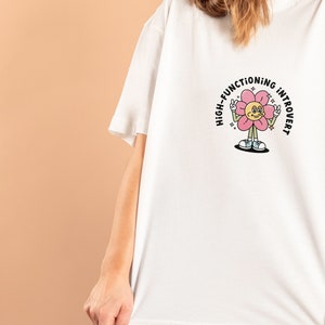 May include: White t-shirt with a pink flower graphic and the text "High-Functioning Introvert".