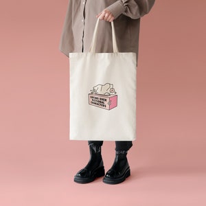 May include: A white tote bag with a pink tissue box and the text "Crying over fictional characters" printed on it.
