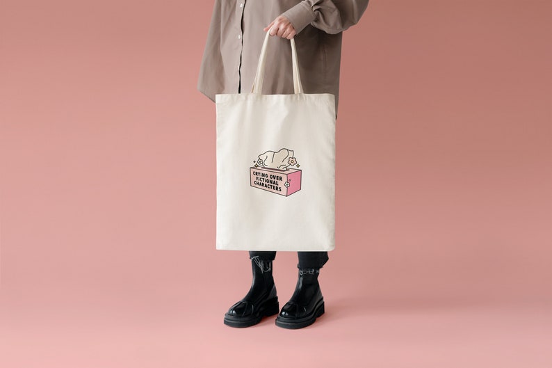 May include: A white tote bag with a pink tissue box and the text "Crying over fictional characters" printed on it.
