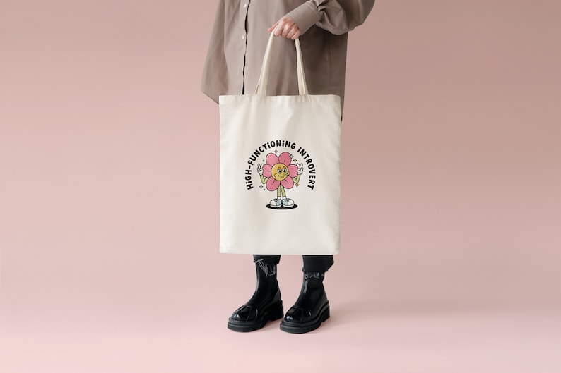 May include: A white tote bag with a pink flower graphic and the text "High-Functioning Introvert".