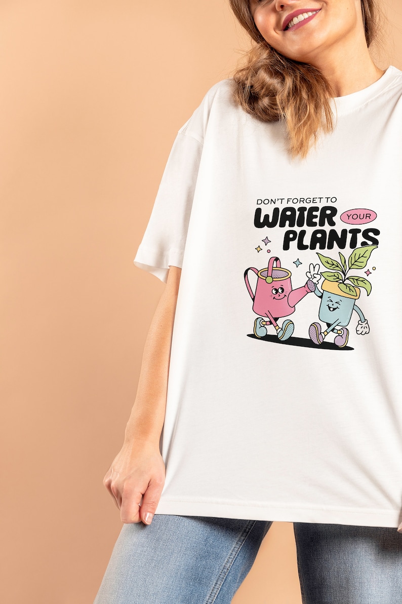 May include: White t-shirt with a graphic of a watering can and a potted plant with the text "Don't forget to water your plants".