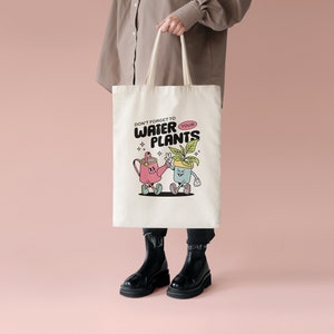 May include: A white tote bag with a cartoon watering can and potted plant design. The text on the bag reads "Don't forget to water your plants".