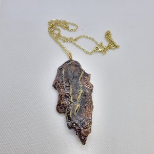 May include: A gold chain necklace with a brown and gold pendant. The pendant is a unique, abstract shape with a textured surface.