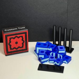May include: A red and black cube with the text "Custom Text" on the top. The cube is made of small squares and has a decorative pattern on the front. There are also blue and light blue blocks with a wavy pattern on them. The blocks are arranged in a pile and are next to a black stand with four black rods.