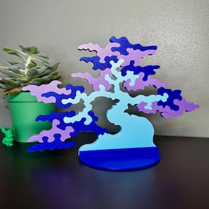 May include: A decorative tree-shaped puzzle featuring interlocking pieces in shades of light blue, medium blue, and lavender. The structure stands on a solid dark blue circular base, showcasing a stylized silhouette with organic, cloud-like foliage.