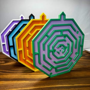 May include: A set of four octagonal maze puzzles arranged in a row. Each puzzle features a distinct color combination: purple and white, blue and black, orange and yellow, and green and lavender. Each maze has a small tab at the top center.