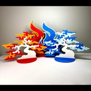 May include: Two decorative tree-shaped sculptures standing on circular bases. The left sculpture features a red and orange gradient with flame-like patterns. The right sculpture features a white and blue gradient with cloud-like patterns.