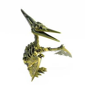 May include: A detailed, metallic gold pterodactyl skeleton figurine. The model features articulated wings and a long beak, with visible rib and bone structure. The figurine is set against a white background, highlighting its intricate design.