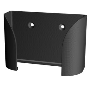May include: Black plastic wall mount with two holes for mounting screws. The mount has a curved design to hold a device.