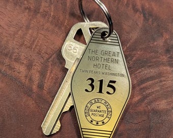 May include: A vintage-style brass key tag and key. The tag reads "THE GREAT NORTHERN HOTEL, Twin Peaks Washington, 315" with a guarantee postage message. The key has the number "65" on it. The key ring is silver.