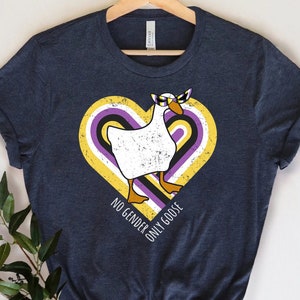 May include: A dark blue t-shirt with a yellow, purple, and white heart design featuring a goose wearing a blindfold. The text "NO GENDER ONLY GOOSE" is printed below the heart.